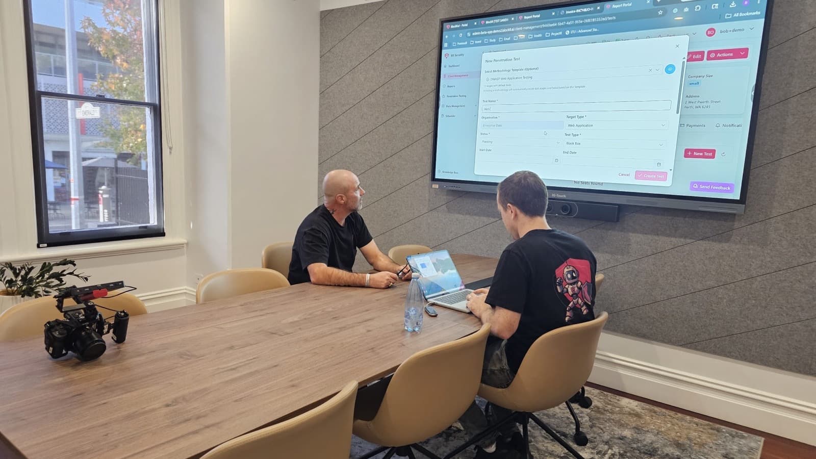 Two Block8.ai team members at a boardroom table, setting up a new penetration test in the Block8 portal on a wall screen